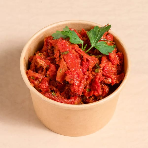 A brown paper cup filled with sun-dried tomatoes and fresh parsley on a light background.