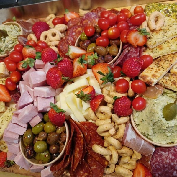 A vibrant charcuterie board with meats, cheeses, olives, cherry tomatoes, strawberries, and focaccia bread.