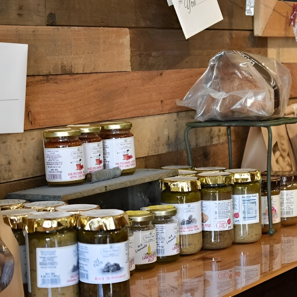 Jars of Altamura Pizza's sauces and spreads, with a loaf of bread, on wooden shelves.