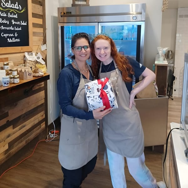 Two smiling Altamura Pizza employees in aprons, one holding a gift, standing in the restaurant.