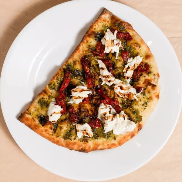 A slice of pesto pizza with sun-dried tomatoes and dollops of fresh mozzarella on a white plate.