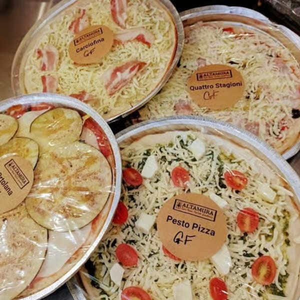 Four Altamura brand gluten-free pizzas, including Carciofina, Quattro Stagioni, Ortolana, and Pesto, in foil pans.
