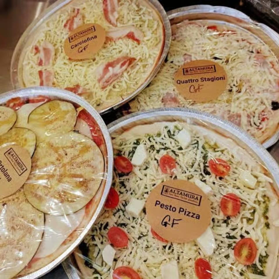 Four Altamura brand gluten-free pizzas, including Carciofina, Quattro Stagioni, Ortolana, and Pesto, in foil pans.
