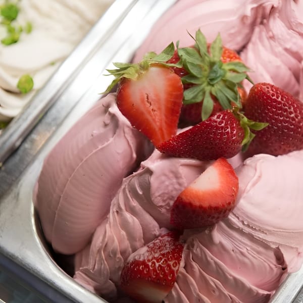 Close-up of strawberry gelato in a metal container, topped with fresh whole and sliced strawberries.