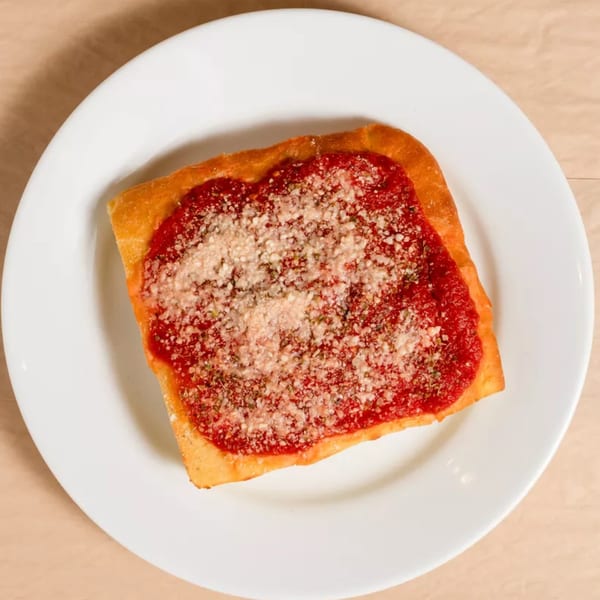A square slice of Detroit-style pizza with red sauce and grated Parmesan cheese on a white plate.