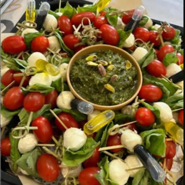Caprese skewers with cherry tomatoes, mozzarella, basil, and a pesto dip with pistachios.