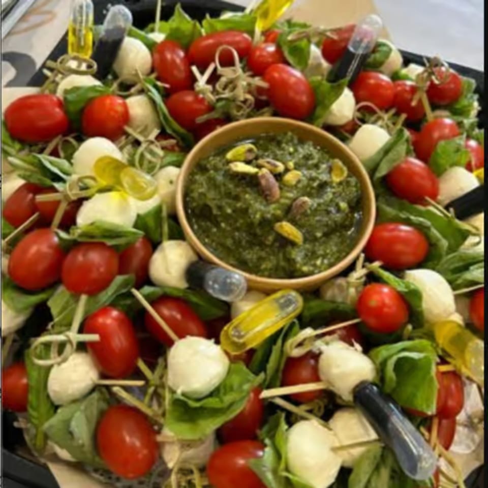 Caprese skewers with cherry tomatoes, mozzarella, basil, and a pesto dip with pistachios.