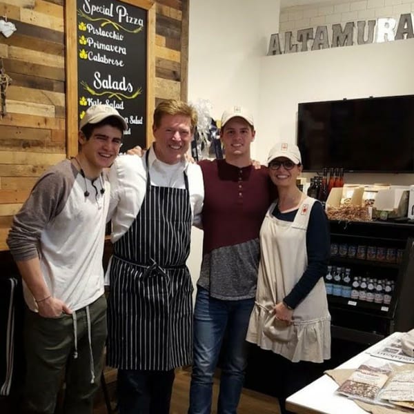 Four smiling people, two men, one boy, and one woman, stand together in a restaurant.