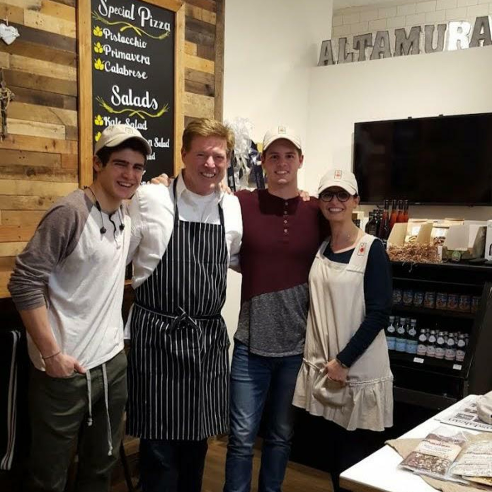 Four smiling people, two men, one boy, and one woman, stand together in a restaurant.