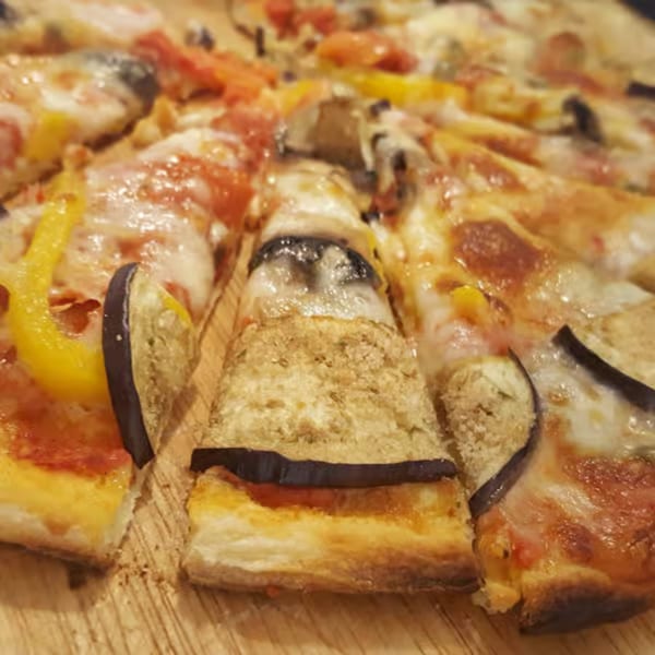 Close-up of a sliced pizza with melted cheese, eggplant, and yellow bell peppers on a wooden board.