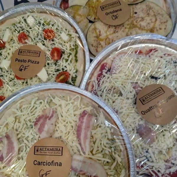 Four Altamura gluten-free pizzas, including Pesto, Ortolana, Quattro Stagioni, and Carciofina, in foil pans.