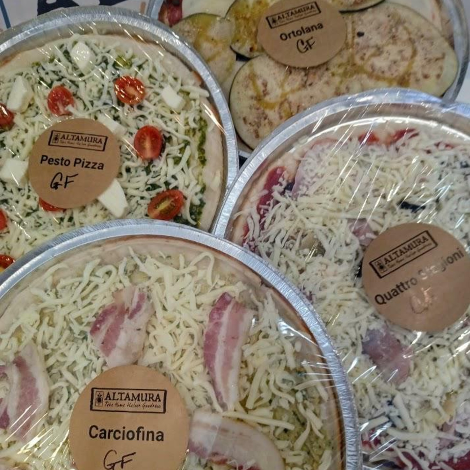 Four Altamura gluten-free pizzas, including Pesto, Ortolana, Quattro Stagioni, and Carciofina, in foil pans.