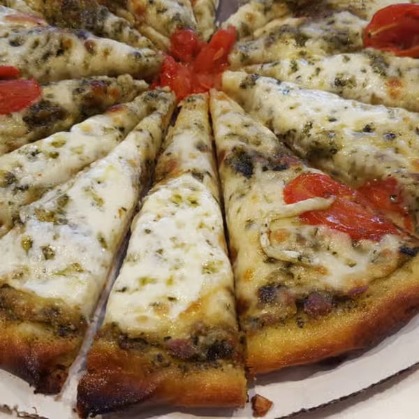 Close-up of a pesto and cheese pizza, cut into slices, with red tomato pieces in the center.