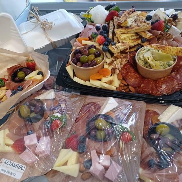 A large charcuterie board with meats, cheeses, olives, fruit, and dips, alongside smaller packaged versions.
