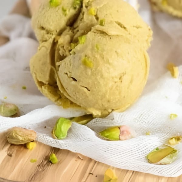 Two scoops of pistachio ice cream with pistachio pieces on a white cloth and wooden surface.