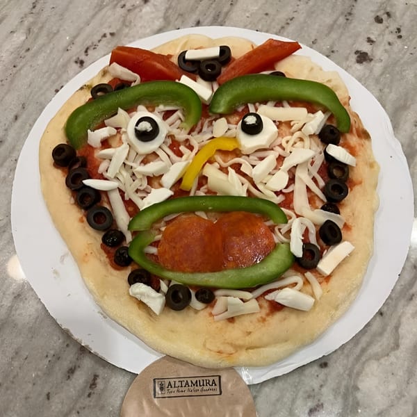 Uncooked Altamura pizza with toppings arranged to look like a face, featuring pepperoni, peppers, and olives.