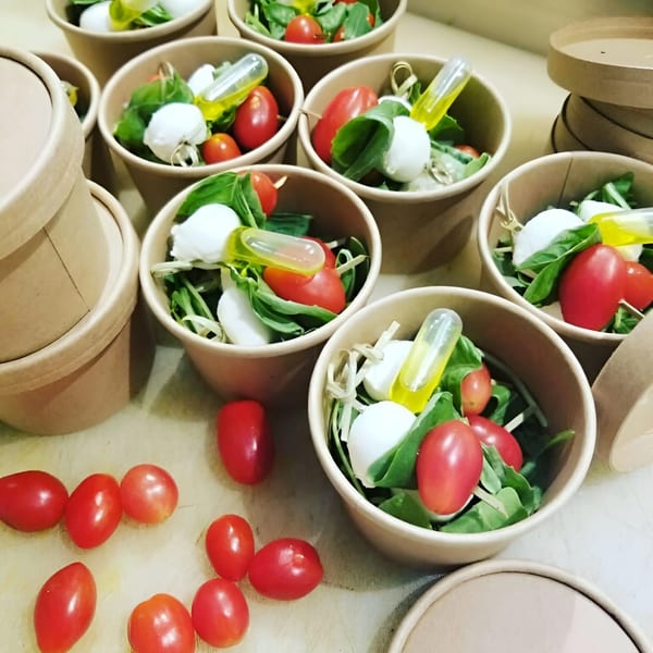 Several individual servings of Caprese salad with cherry tomatoes, mozzarella, and basil in paper cups.