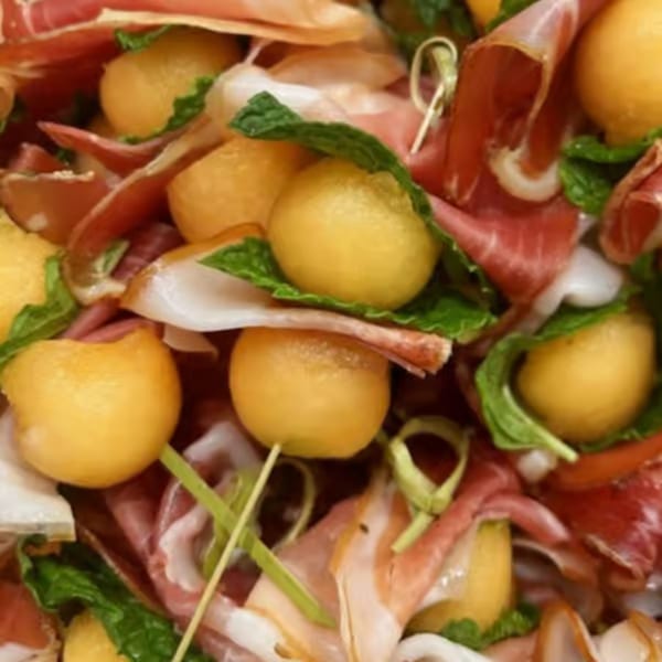 Close-up of prosciutto-wrapped melon balls with fresh mint and green garnish.
