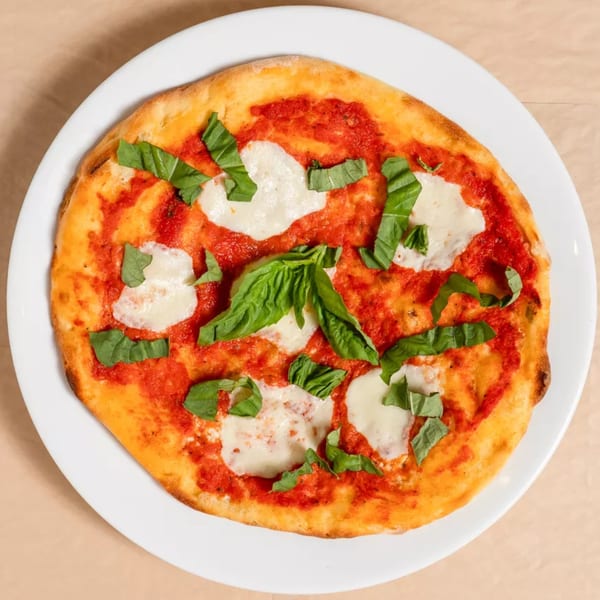 A round Margherita pizza with tomato sauce, fresh mozzarella, and basil leaves on a white plate.