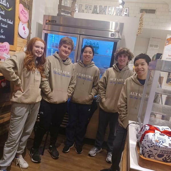 Five smiling young people in Altamura branded hoodies stand in front of a refrigerator.